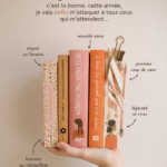 Femme lisant un livre avec une tasse de thé à la main, entourée de livres empilés.